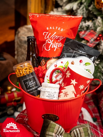 Panier garni avec chips, tasse festive, bière et snacks salés.